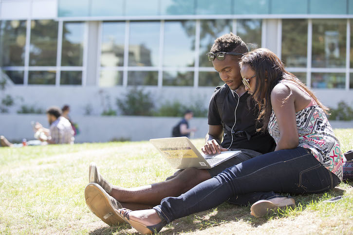 Two student sitting in the grass looking at a computer